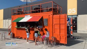 Chiosco bar rosso con terrazza panoramica e apertura lato lungo con portelloni da container sul lato corto